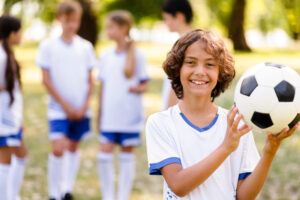 smiling kid holding a soccer ball for sports injuries in kids article