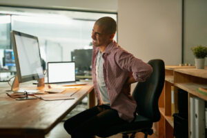 guy winicng in pain sitting in chair because of not improving posture and chiropractic care